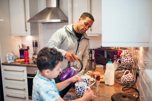 Little boy and his father are making tea for breakfast at home.