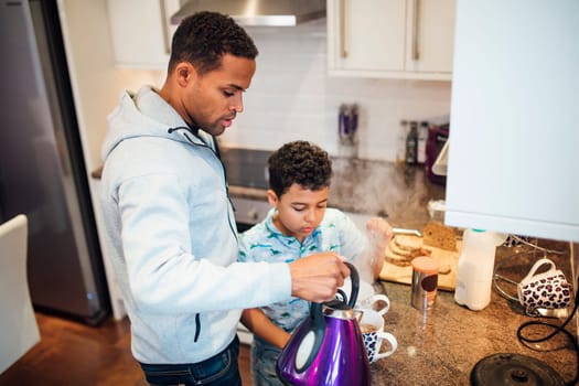 Little boy is helping his father while he makes tea in the morning.