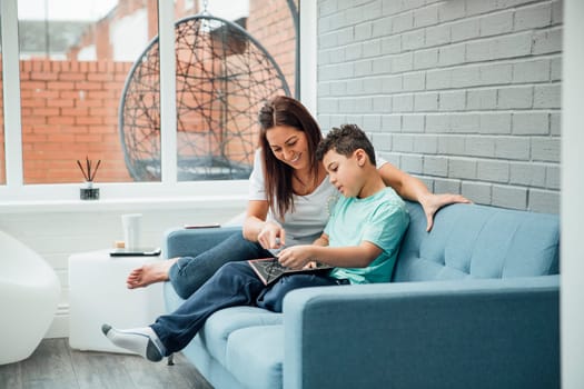 Little boy and his mother are reading a book together in the conservatory of their home.