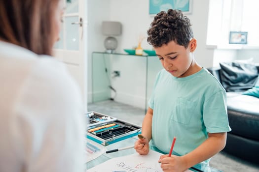 Little boy and his mother are making a Father's Day card at home using crayons and paints.