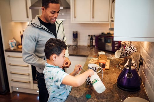 Little boy and his father are making tea for breakfast at home.