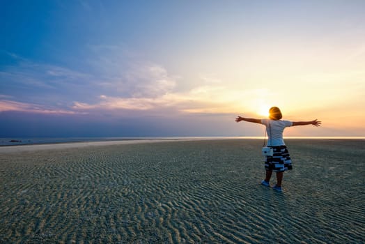 Happy woman tourist standing arms outstretched on the beach watching the beautiful natural landscape of colorful sky and sea during sunset at Nathon Sunset Viewpoint in Samui island, Surat Thani, Thailand