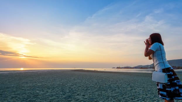 Happy women tourist raise hands at the mouth yelling and beautiful natural landscape of colorful sky and sea during a sunset at Nathon Sunset Viewpoint in Samui island, Surat Thani, Thailand, 16:9 widescreen