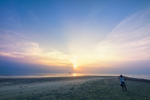 Asian woman tourist taking photo on the beach and beautiful natural landscape of colorful sky and sea during a sunset at Nathon Sunset Viewpoint in Samui island, Surat Thani, Thailand