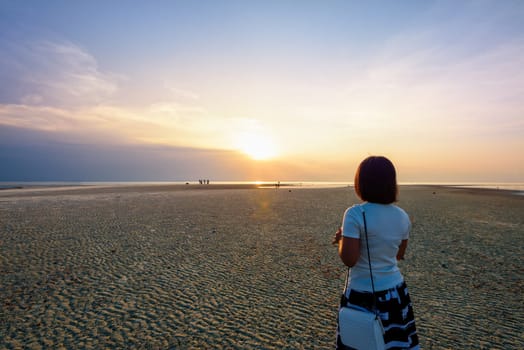 Women tourist standing on the beach watching the beautiful natural landscape, colorful of the sky and the sea during a sunset at Nathon Sunset Viewpoint in Ko Samui island, Surat Thani, Thailand