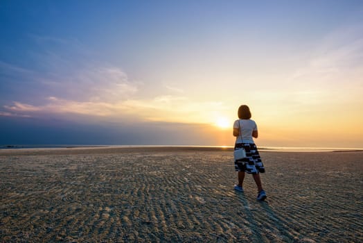 Young woman tourist strolling on the beach watching the beautiful natural landscape, colorful of the sky and the sea during a sunset at Nathon Sunset Viewpoint in Ko Samui, Surat Thani, Thailand
