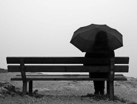 Woman with an umbrella sitting on a bench at a cliff edge