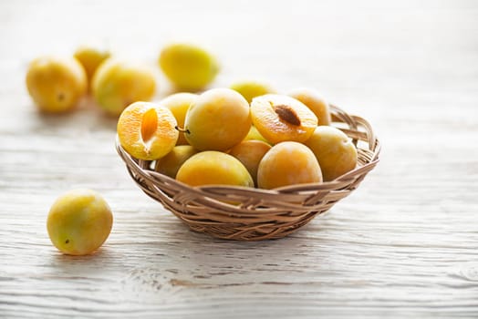 Yellow plums with leaves in a basket on old wooden background close up