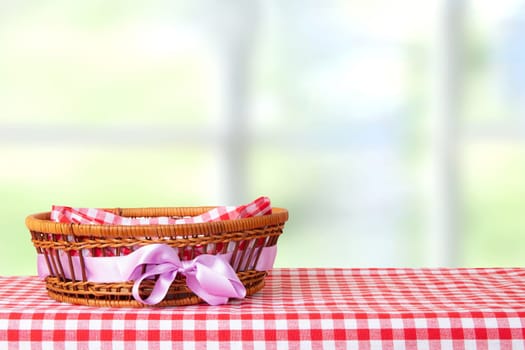 Empty basket with purple ribbon on red checkered tablecloth with bright pastel color background. For your food and product display montage.