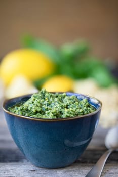 Bowl of fresh pesto with ingredients in background, vertical orientation with copy space.