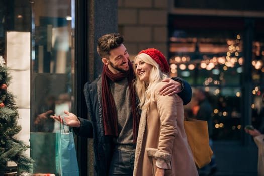 Side view of a couple looking through a store window while christmas shopping together.