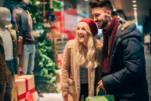 Side view of a couple looking with excitement through a shop window while looking for items to buy.
