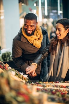 Front view of a couple standing at a christmas market stall deciding on what wreath they should buy.