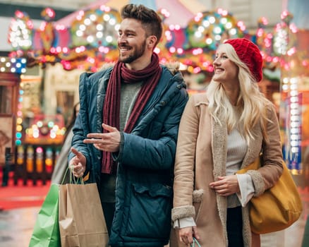 Waist up, front view of a couple walking on a city street with shopping bags in their hand.