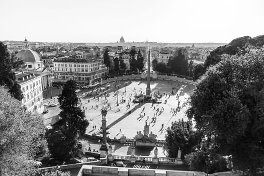 Aerial view of people, sculptures, fountain and churches on Piazza del Popolo in Rome, Italy. Black and white image.