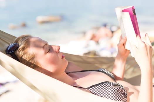 Woman reading book in hammock on the beach. Summertime read.