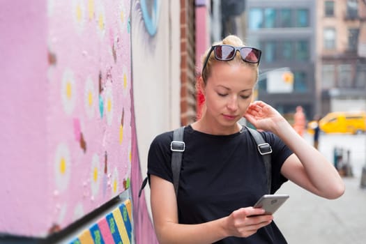 Closeup of female hipster with smart phone. Woman using smartphone against colorful graffiti wall in East Village, New York city, USA.