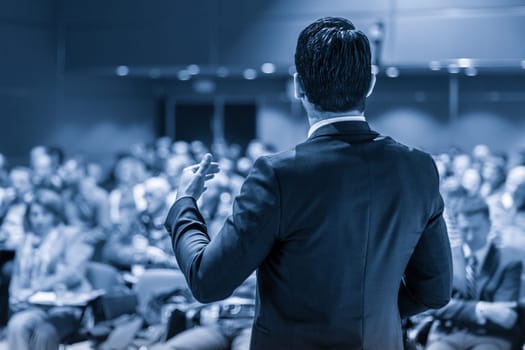 Speaker giving a talk on corporate business conference. Unrecognizable people in audience at conference hall. Business and Entrepreneurship event. Blue toned grayscale image.