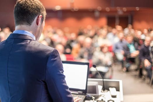 Speaker giving a talk on corporate business conference. Unrecognizable people in audience at conference hall. Business and Entrepreneurship event.