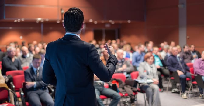Speaker giving a talk on corporate business conference. Unrecognizable people in audience at conference hall. Business and Entrepreneurship event.