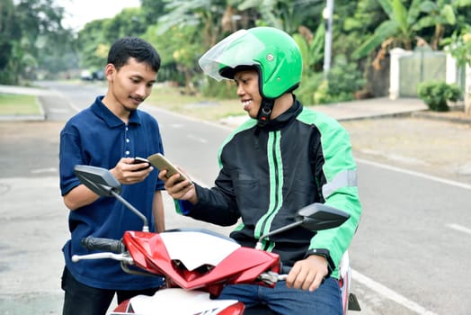 Happy asian man ordering motorcycle taxi by mobile phone on the sidewalk