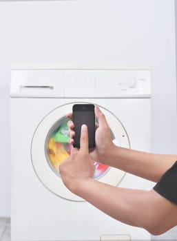 Male hand operate washing machine with his mobile phone. Home appliance