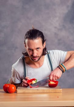 young bearded man cutting sweet pepper in front of gray background
