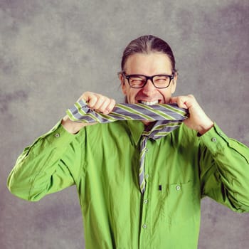 stressed man in green shirt and glasses biting in his  necktie and looking crazy in to the camera