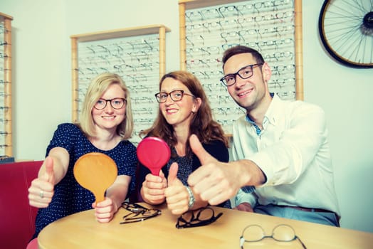 in optician shop-two women and one man with thumb up selecting new glasses