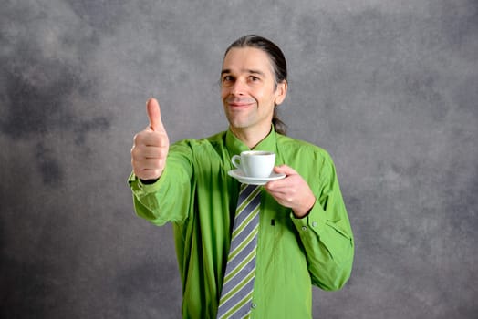 young man in green shirt and necktie drinking coffee and showing thumb up