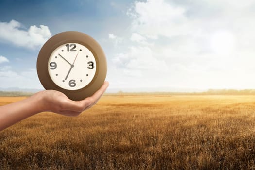 Man holding a clock with dry grass field background. Time to Harvest Fall Day