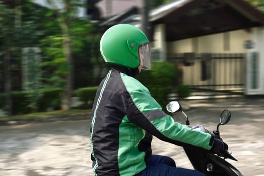 Young motorcycle taxi driver with green helmet on the city
