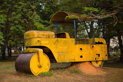 Old rusty yellow road roller in rural scene.