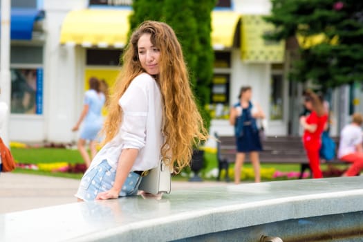 Beautiful young girl examines passers by the fountain in the park