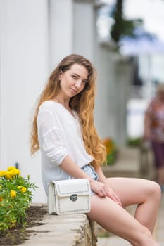 A young girl with a lady's white handbag crouched on the parapet and looked at the frame