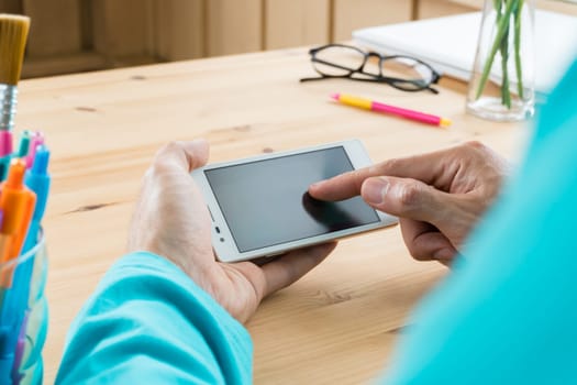 Green t-shirt businessman touching screen of smartphone or mobile phone in home office. Smartphone or mobile phone and pen and laptop and eyeglasses. Social or internet and technology communication concept