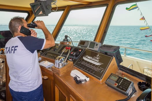 Captain in the post of a ship watching with binoculars on the Adriatic Sea along the town of Igea Marina near Rimini in Italy