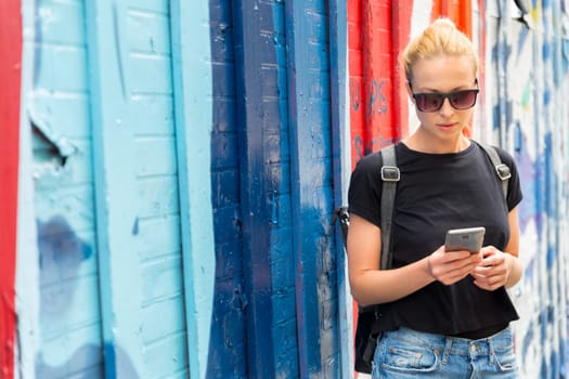 Closeup of female hipster with smart phone. Woman using smartphone against colorful graffiti wall in East Village, New York city, USA.