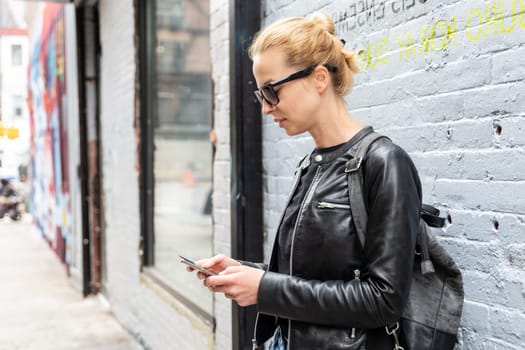 Closeup of female hipster with smart phone. Woman using smartphone against colorful graffiti wall in East Village, New York city, USA.