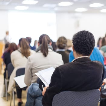 Business and entrepreneurship symposium. Female speaker giving a talk at business meeting. Audience in conference hall. Rear view of unrecognized participant in audience. Copy space on whitescreen.