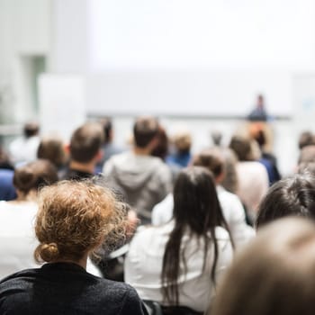 Female speaker giving presentation in lecture hall at university workshop. Audience in conference hall. Rear view of unrecognized participant in audience. Scientific conference event.