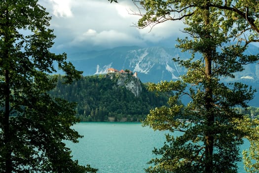 Bled castle between trees over the lake cloudy weather