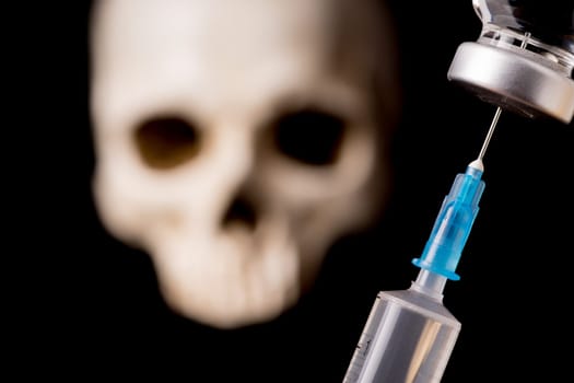 medical vials, syringe and blurry skull isolated on black background