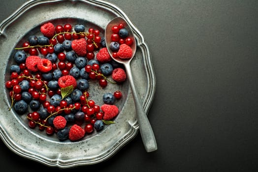 Mix of fresh berries in a plate on black background