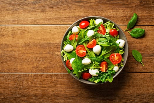Green lettuce Salad with mozzarella cheese arugula and tomato on wooden background