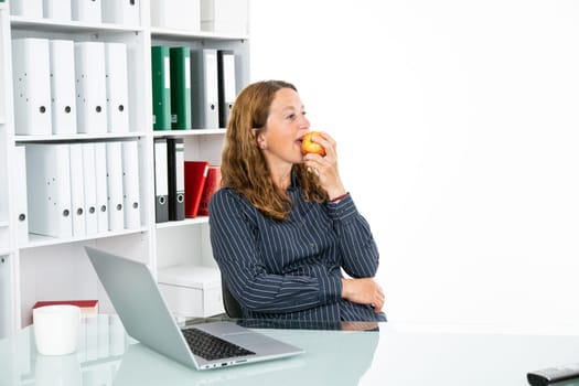 brown-haired blond businesswoman eating apple in the office