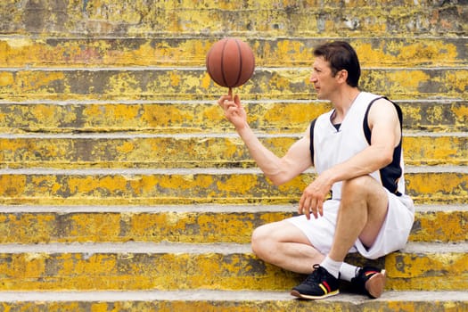 The playful basketball player is turning ball around on one finger and sitting on the stairs.