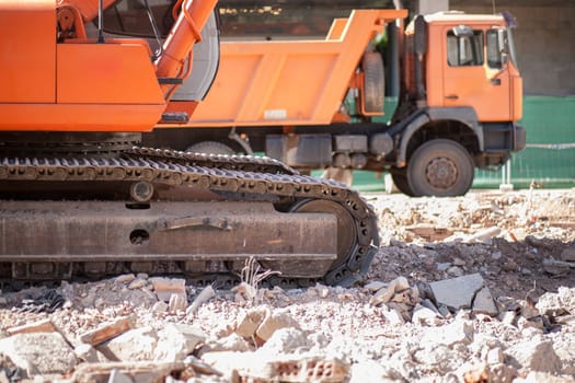 Track excavator and dump truck over loads of brick rubble debris. Construction site