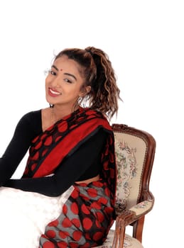 A gorgeous young East Indian teenager sitting in an old armchair in a .colorful Indian saree, smiling, isolated for white background.