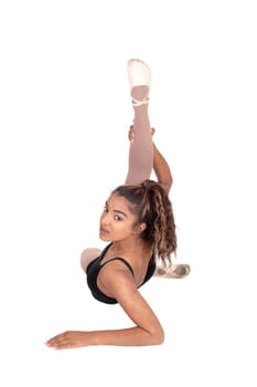 A slim young woman in an ballet outfit sitting on the floor with one.leg up doing warm up exercises, isolated for white background.